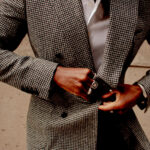 Portrait of Denzel Coke, who wears a houndstooth jacket and several bold rings.