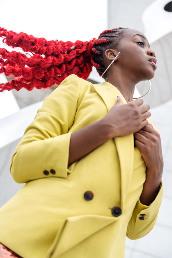 Close-up of a black woman flipping her curly red ponytail, wearing a lime blazer