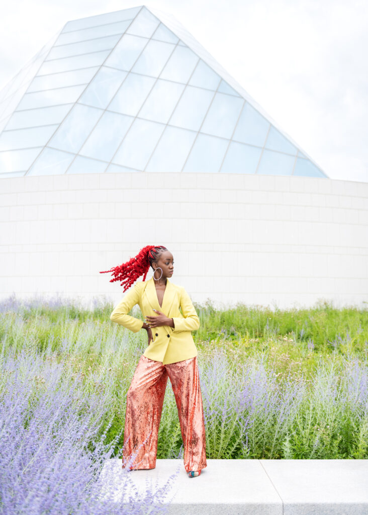 A black woman flipping her red ponytail, posing among lavender plants and greenery