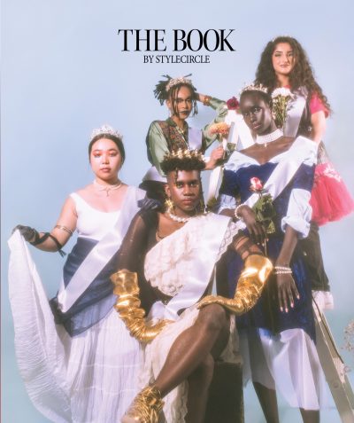 Five people in crowns and sashes are posed in front of a white backdrop on the cover of The Book 08, themed Give Them Their Flowers.